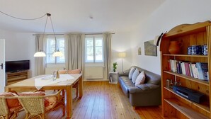 Tunnelmallinen olohuone, jossa on puulattia, ruokapöytä tuoleineen, sohva, kirjahylly ja televisio.