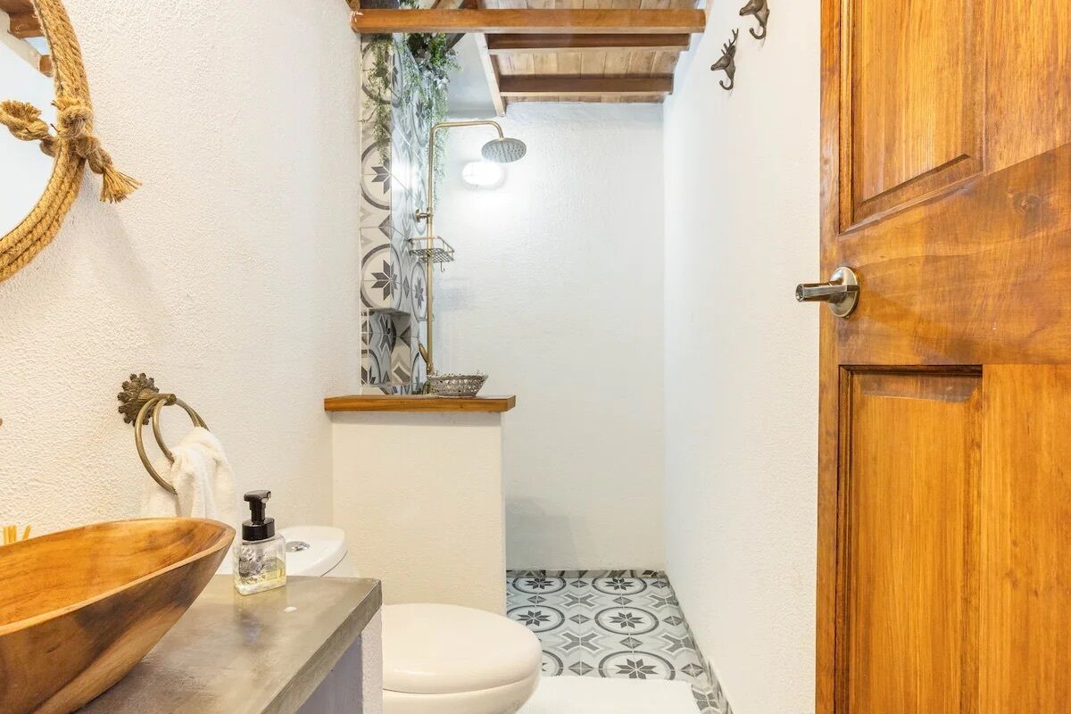 Un baño con lavamanos de madera, inodoro y ducha con piso de baldosas estampadas.