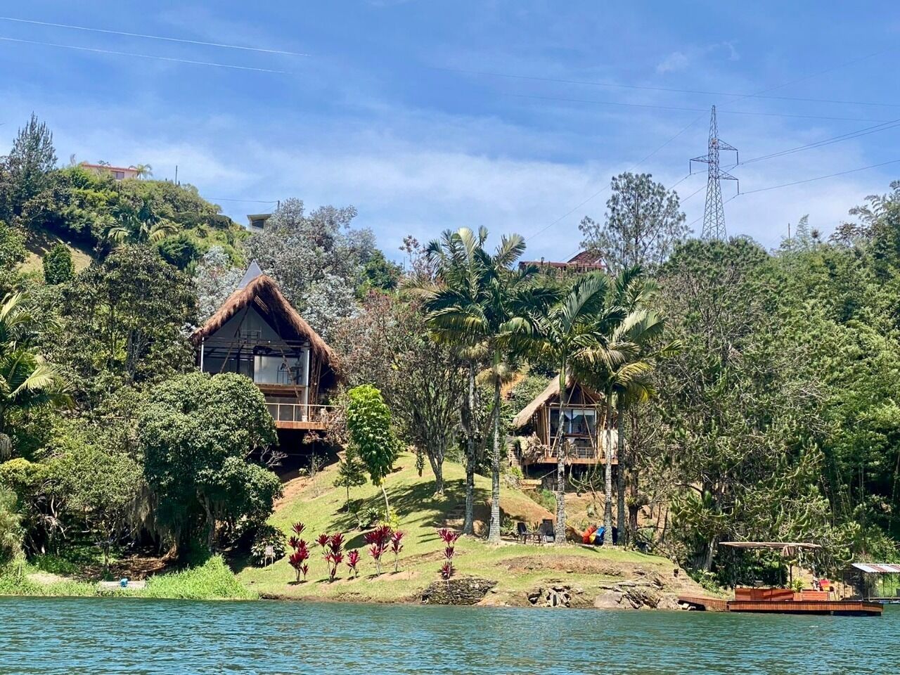 A tropical resort with thatched-roof cabins, lush greenery, and a calm lake.