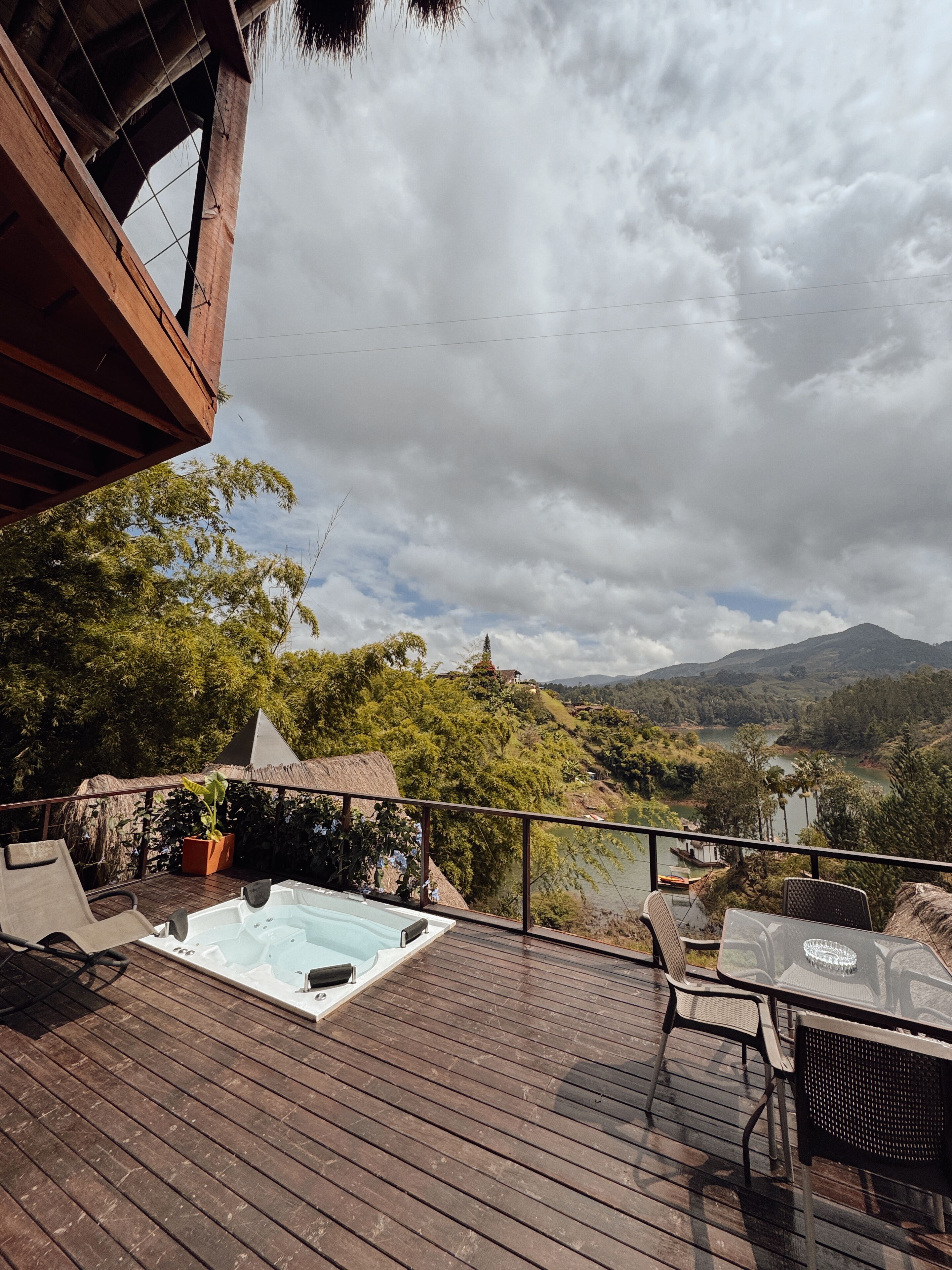 Una terraza de madera con un jacuzzi, mobiliario exterior y vistas a un valle con montañas.
