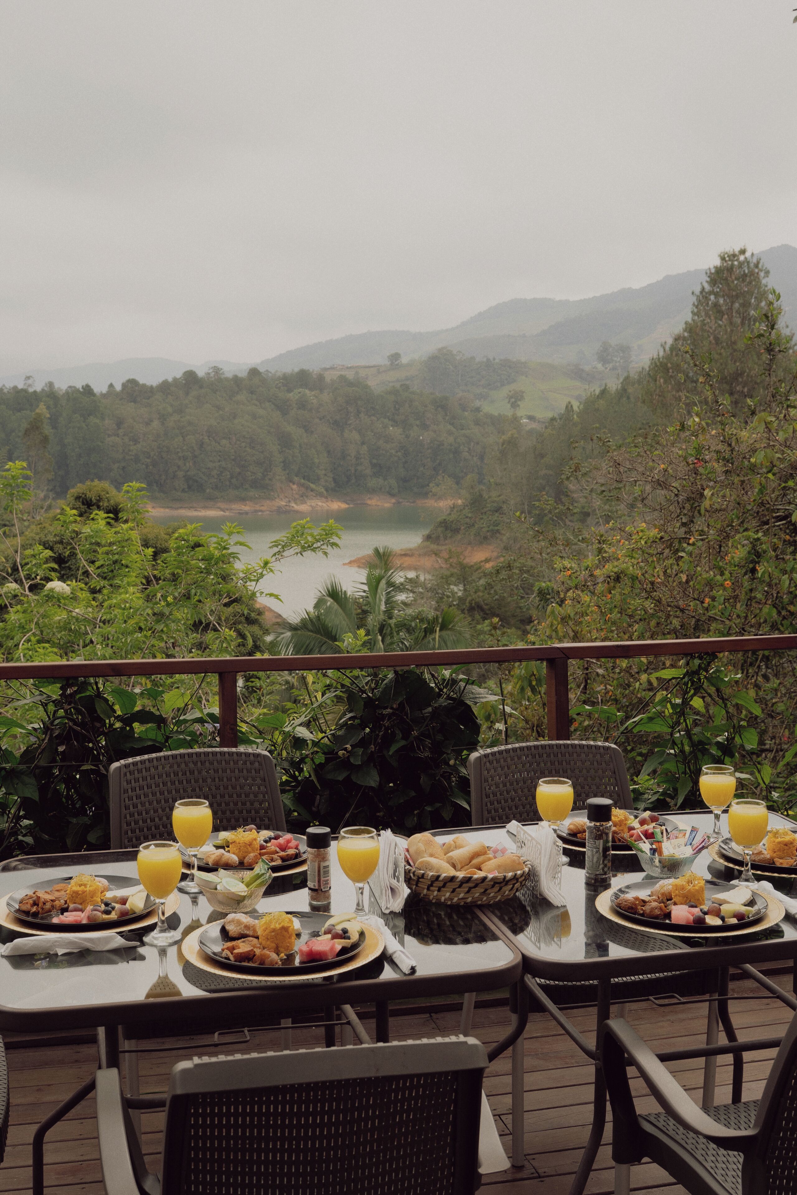 A breakfast table set with plates of food, glasses of orange juice, and a view of a river and hills.
