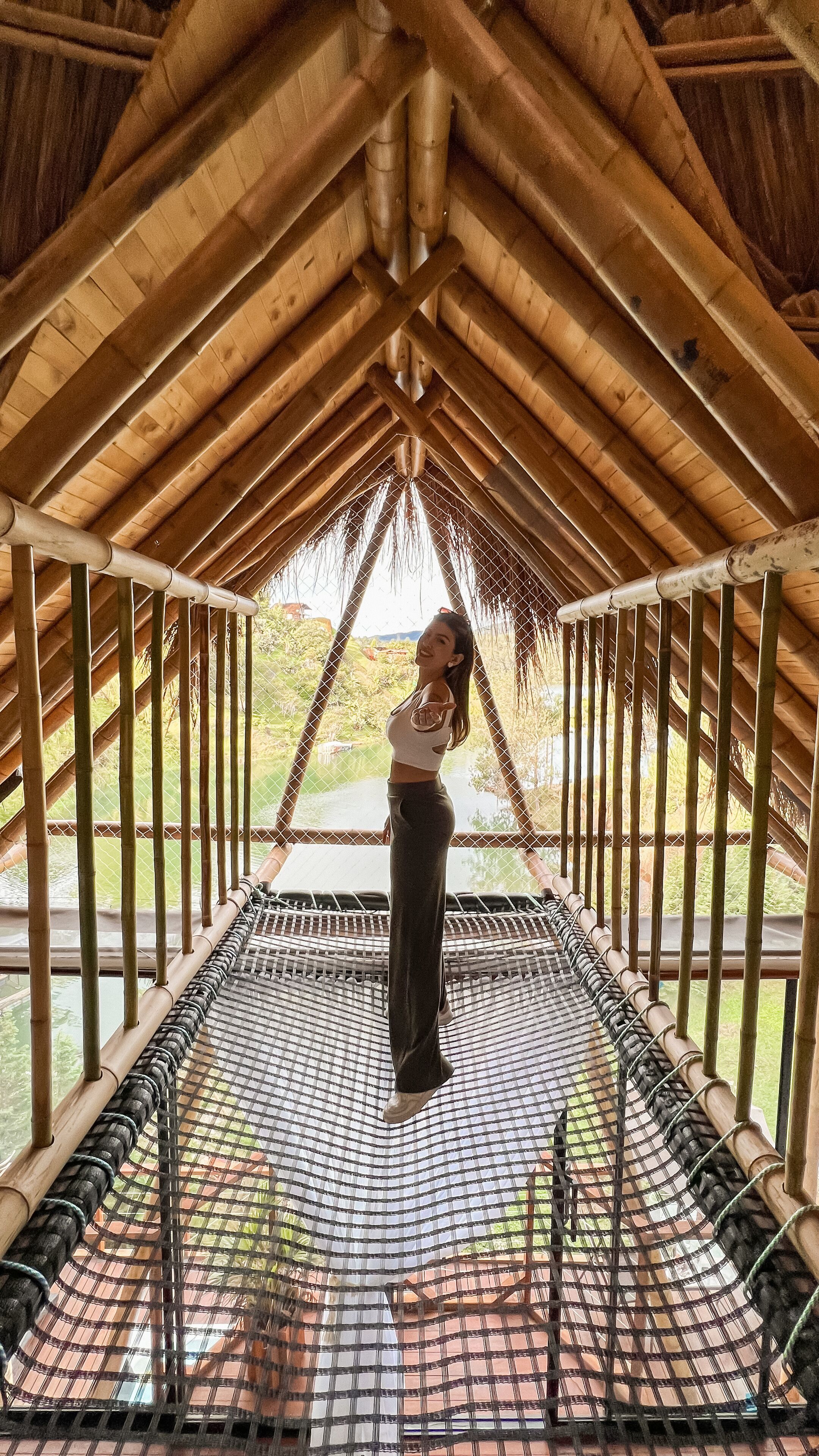 A person standing on a netted platform inside a wooden structure with a view of greenery and water outside.