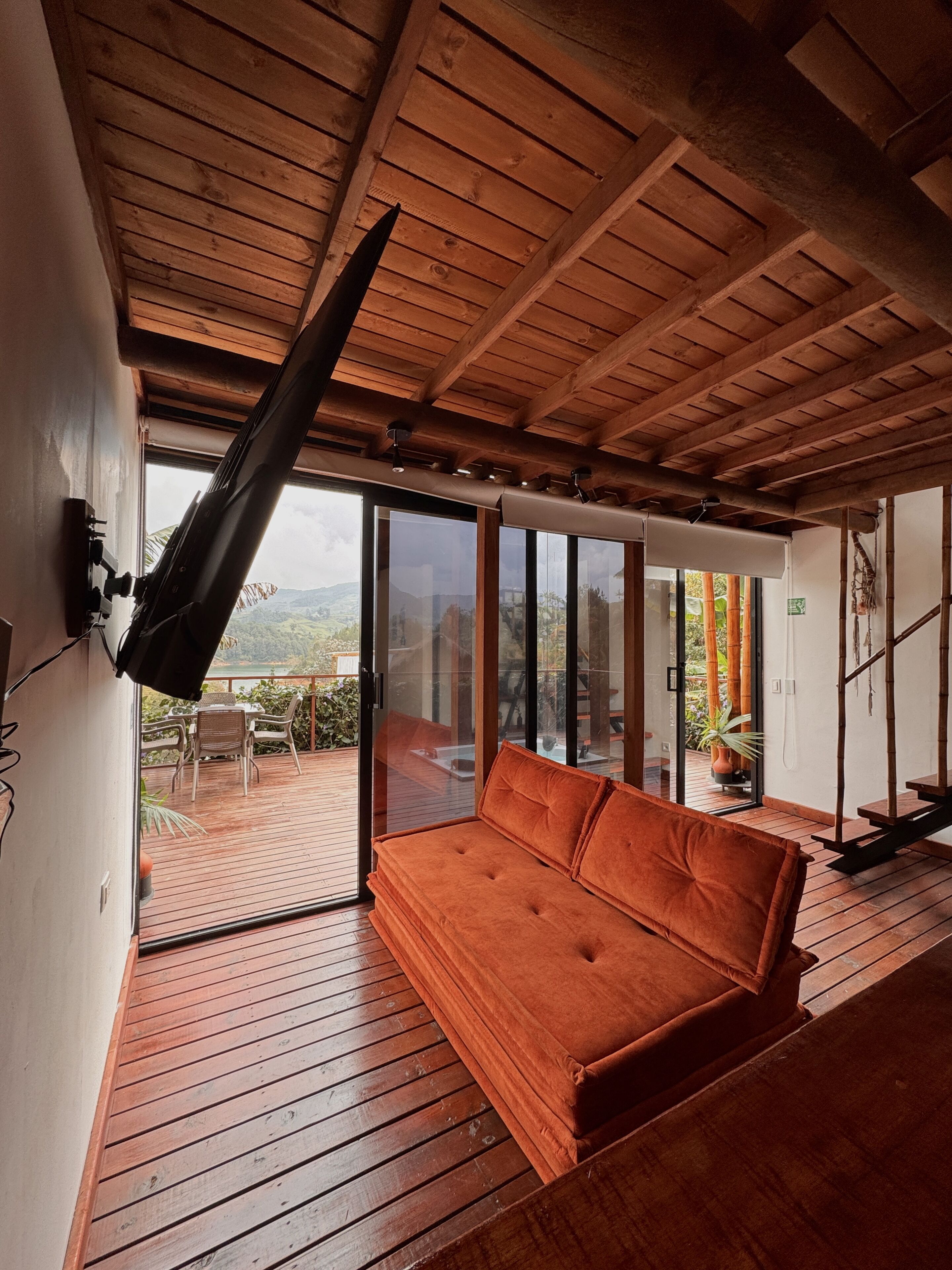 A room with a wooden ceiling, a sofa, and a sliding glass door leading to an outdoor area with a view of mountains.