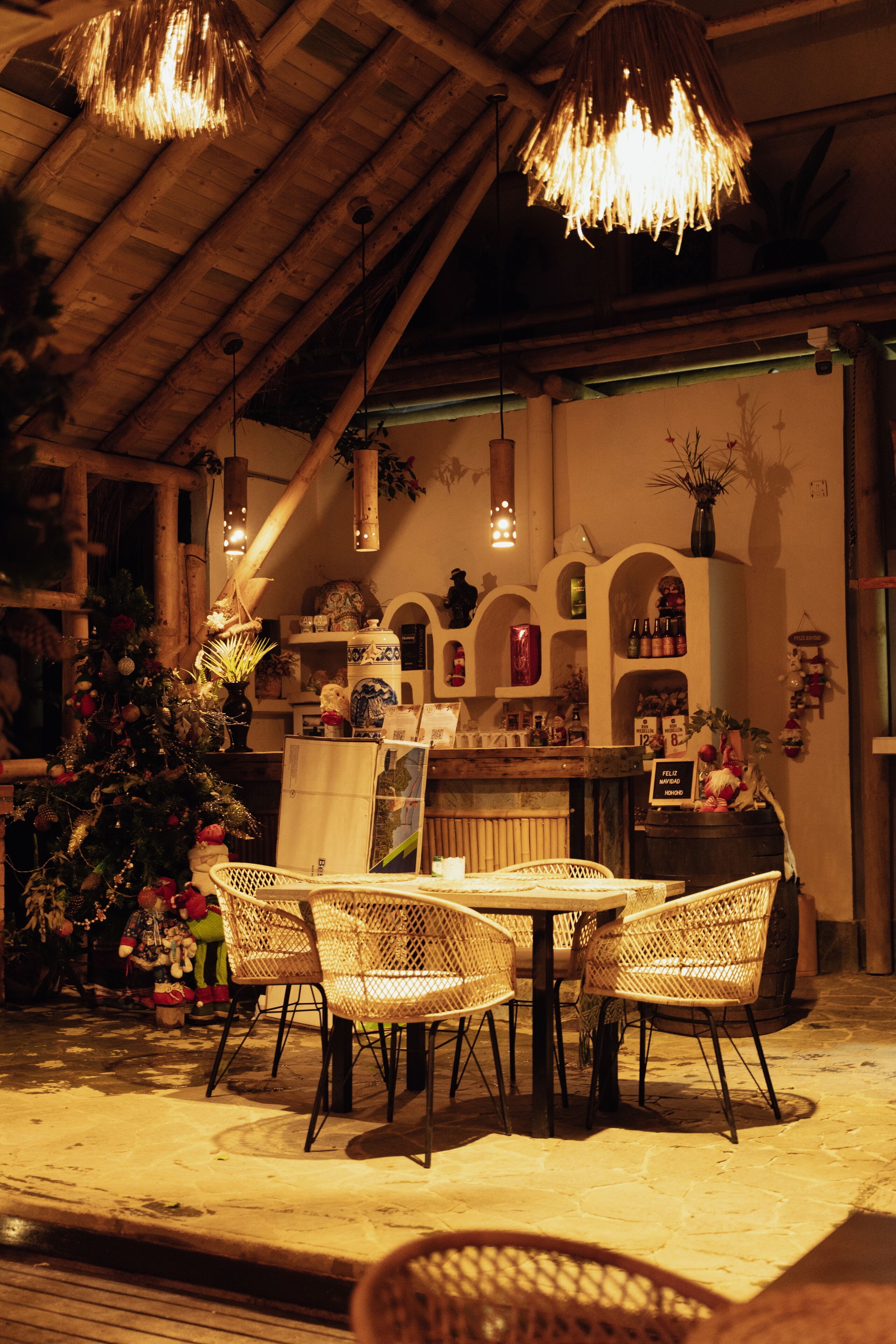 A cozy indoor setting with wicker chairs around a table, a Christmas tree, and a bar area with shelves and decorative items.