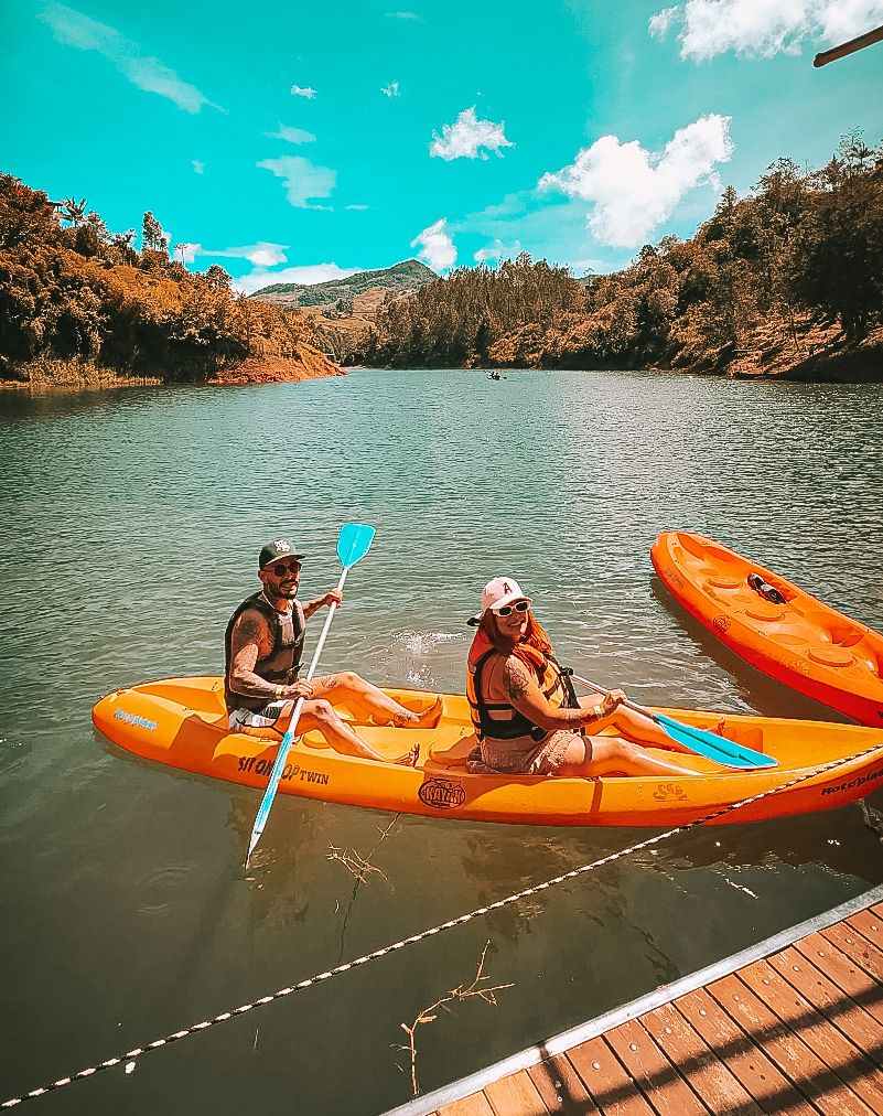 Two people in a kayak on calm water, with a dock in the foreground and trees in the background.