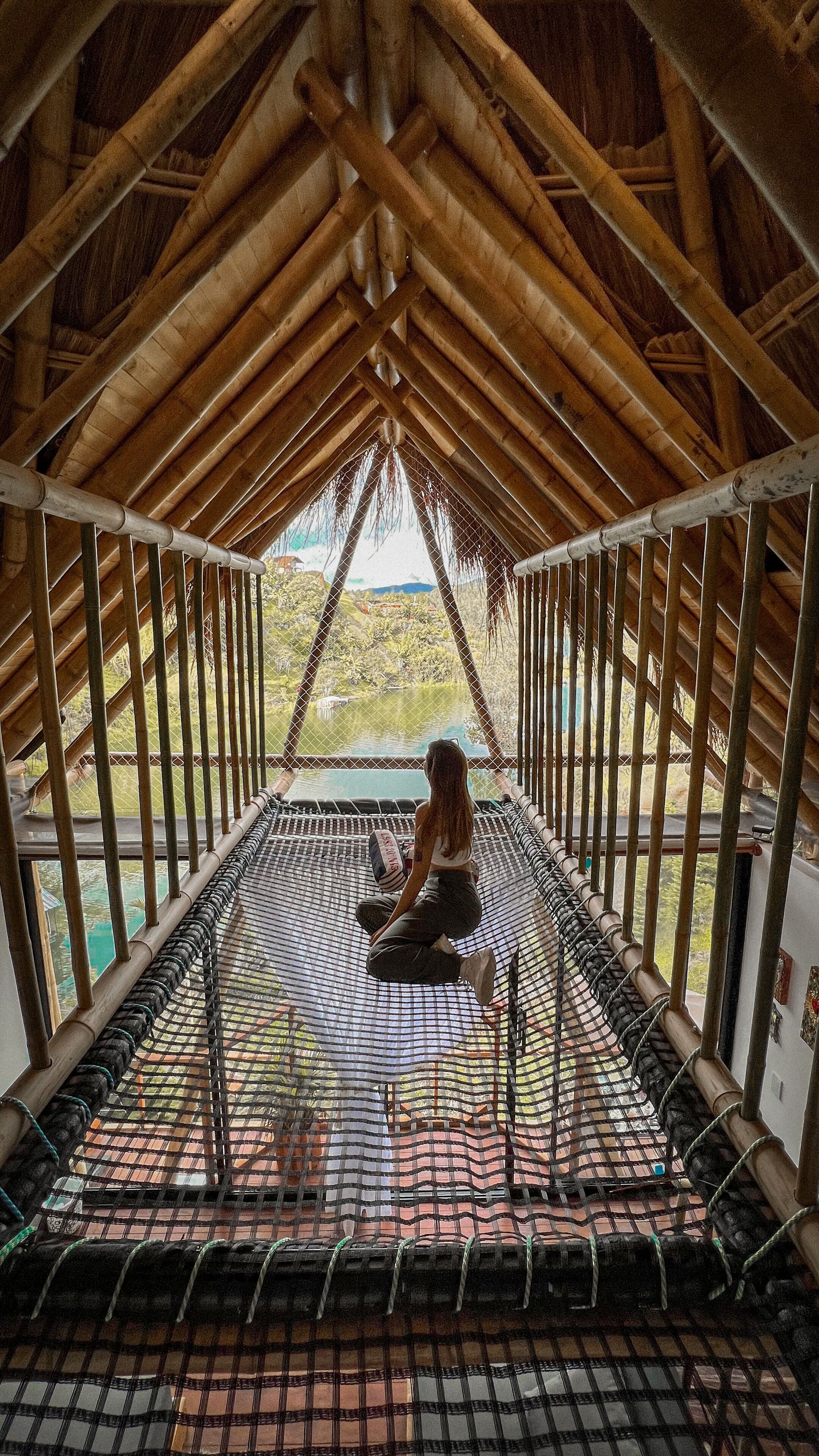 A person sitting on a hammock in a wooden-roofed room with a view of a lake.
