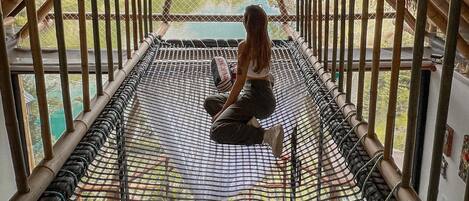 A person sitting on a hammock in a wooden-roofed room with a view of a lake.