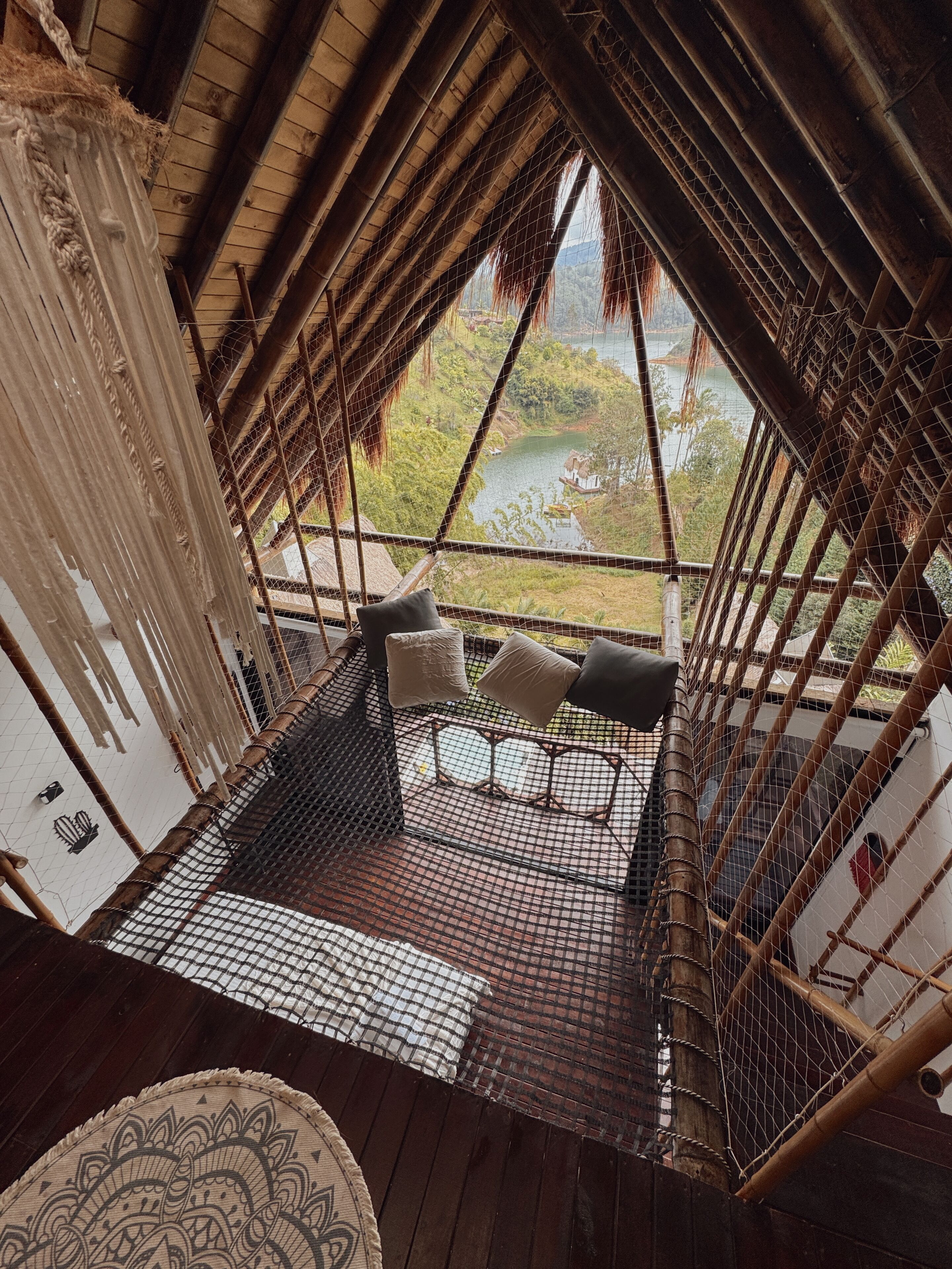 Una habitación con techos altos, una hamaca, un tapiz decorado y vistas a un río y follaje.