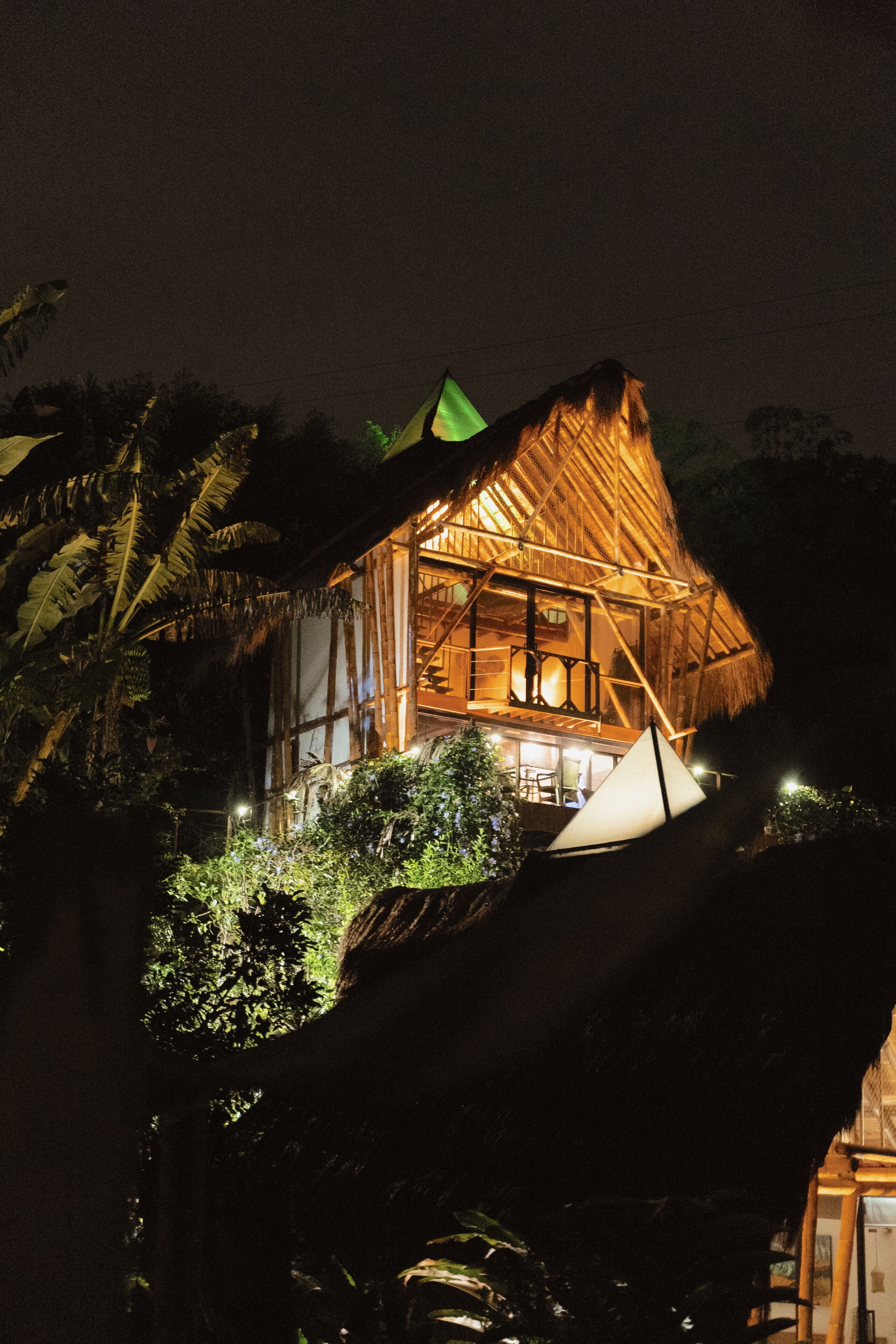 Um edifício com telhado de palha e varanda, rodeado por vegetação exuberante.