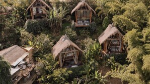 A resort with thatched-roof cabins surrounded by lush vegetation. - Ibuku Hotel (El Peñol)