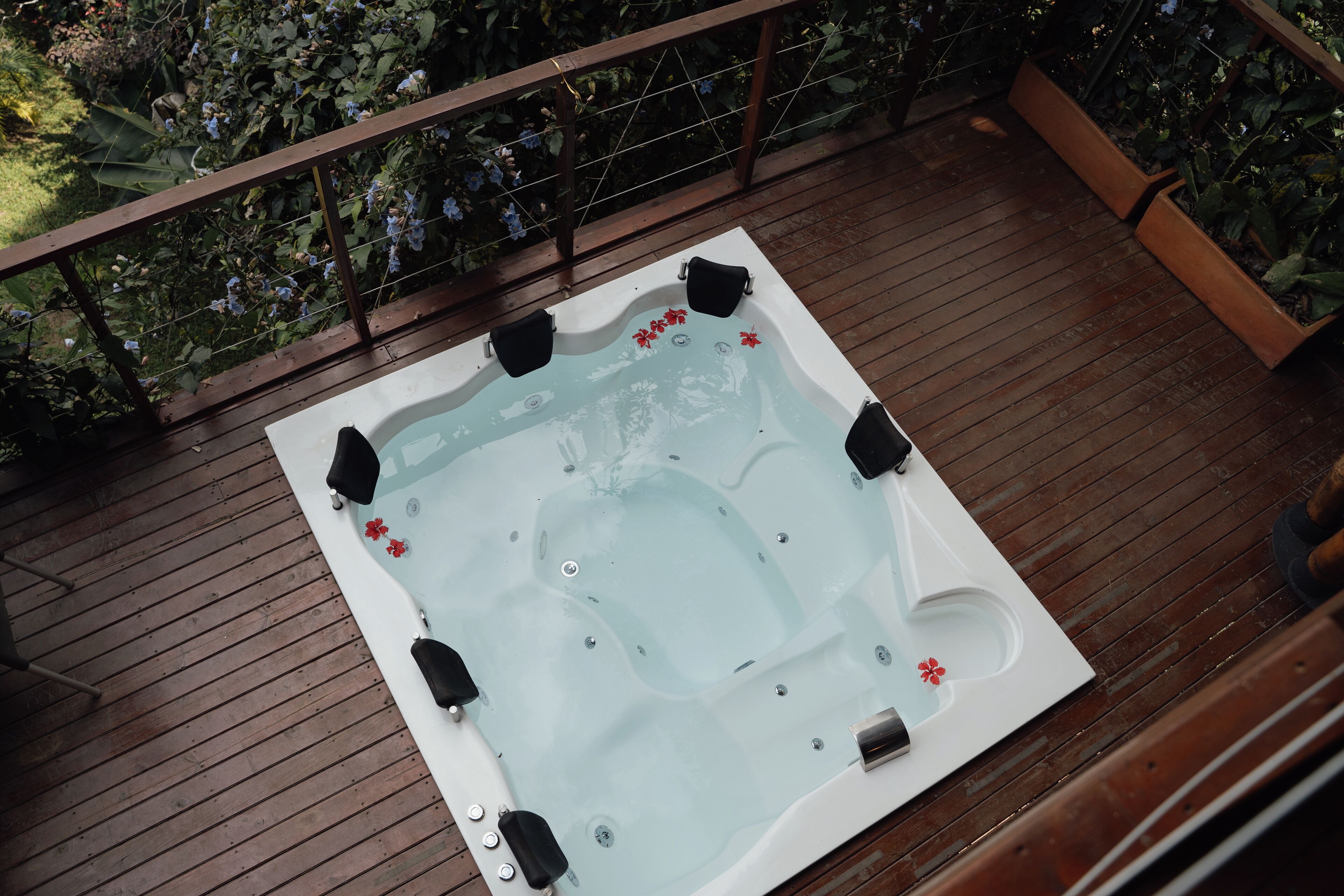 A hot tub on a wooden deck with a wooden railing and plants in the background.