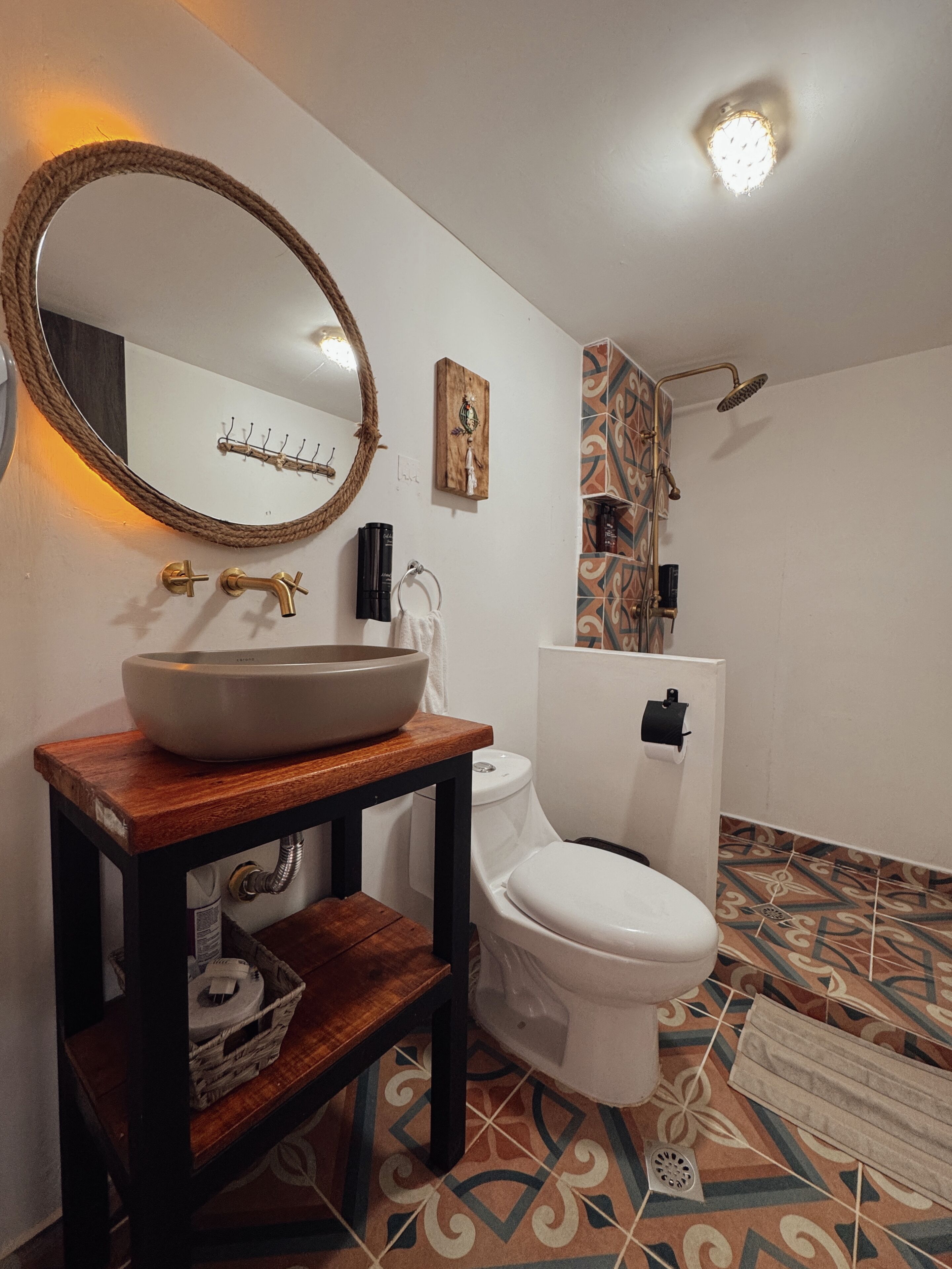A bathroom with a round mirror, a wooden vanity, a toilet, and a shower area.