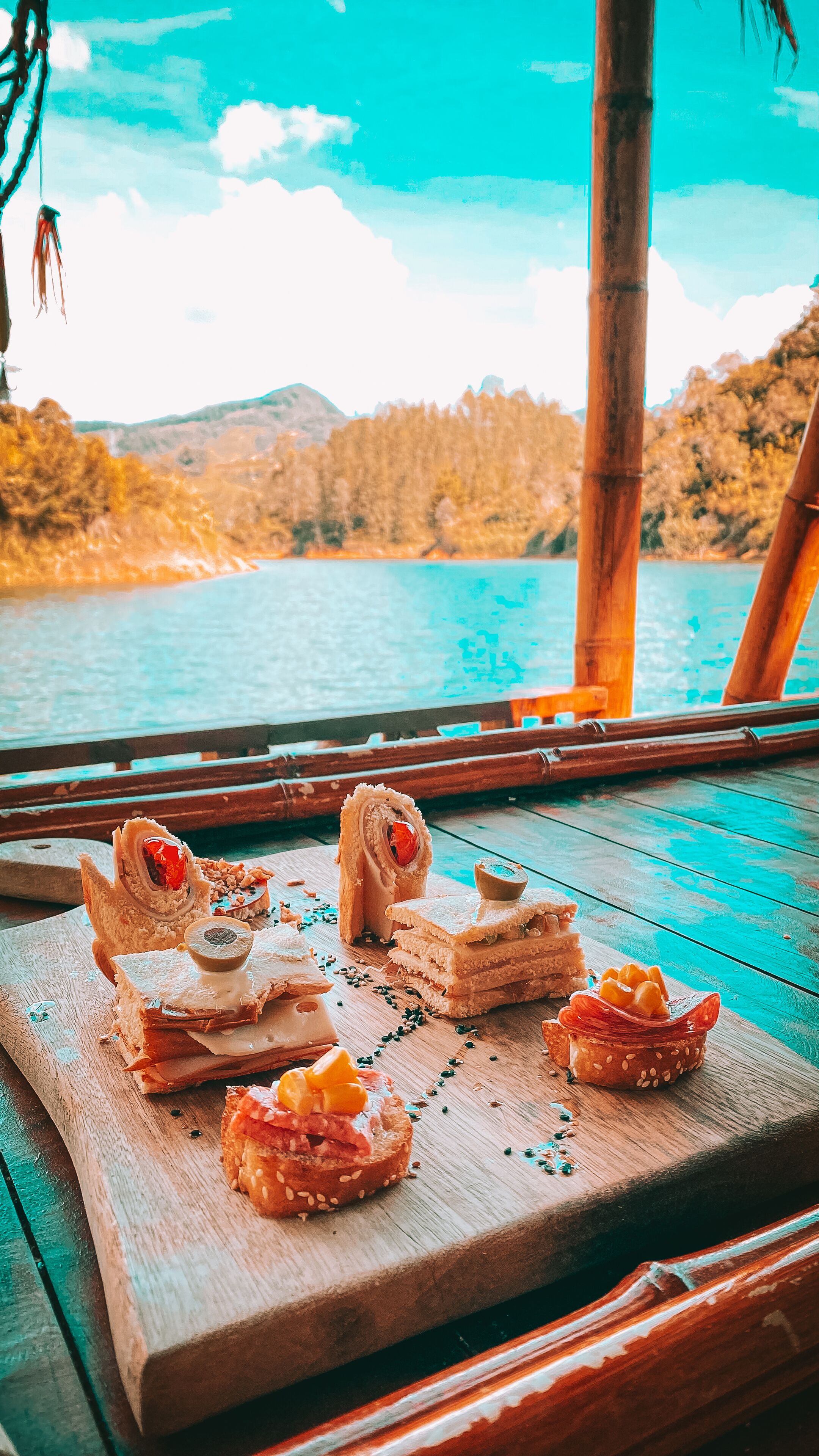 Una mesa de madera con diversos alimentos, vista a un lago y un paisaje boscoso.