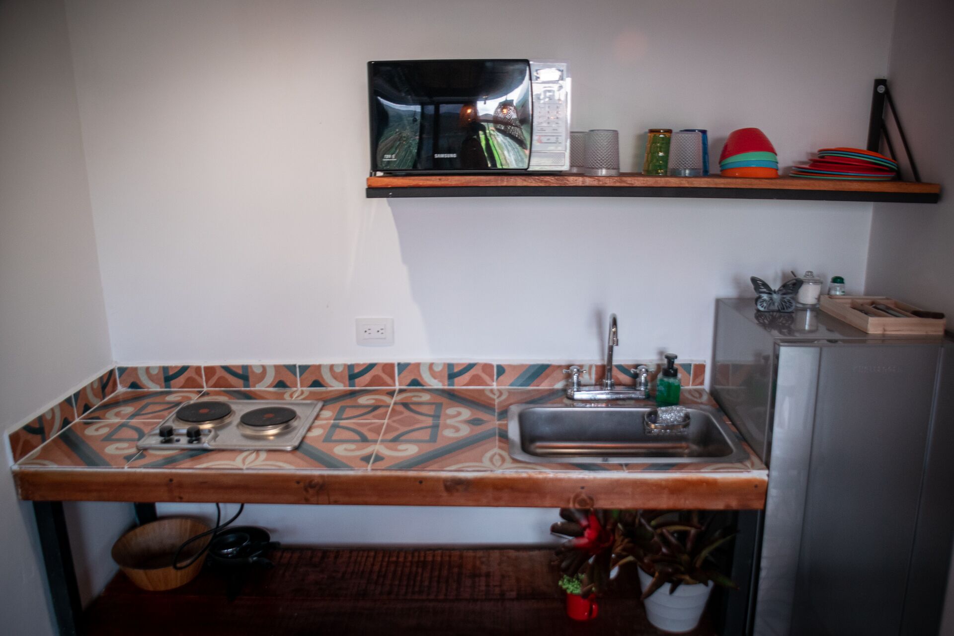 A kitchen with a patterned backsplash, a stove, a sink, and a microwave on a shelf.