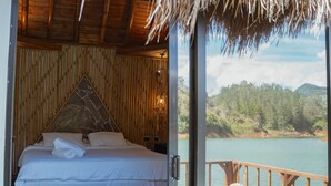 A room with a bed, a bamboo wall, and a view of a lake. - Ibuku Hotel (El Peñol)