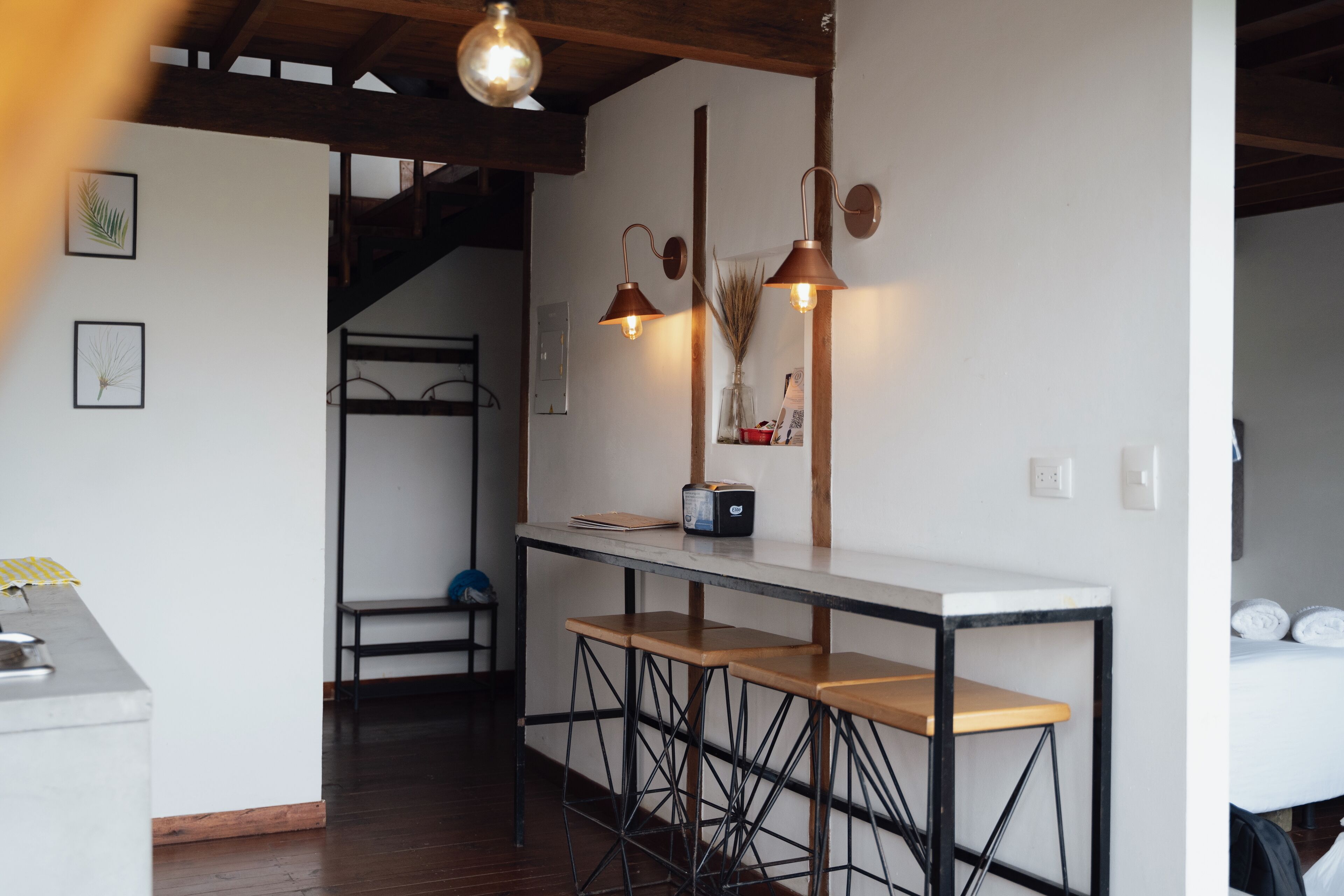 Una cocina moderna con encimera blanca, taburetes de madera e iluminación colgante.