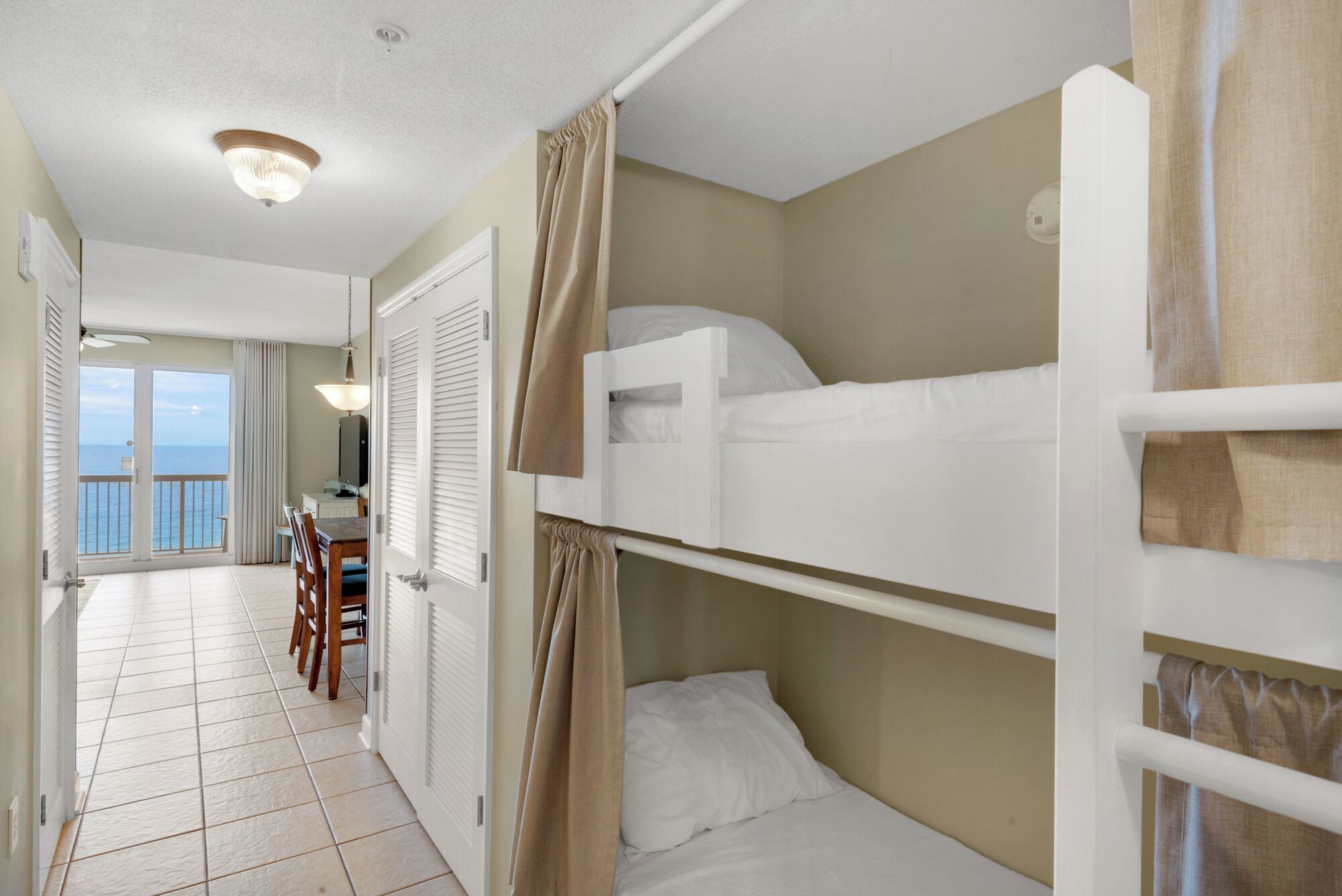 A room with bunk beds, a door leading to a balcony, and a view of the sea.