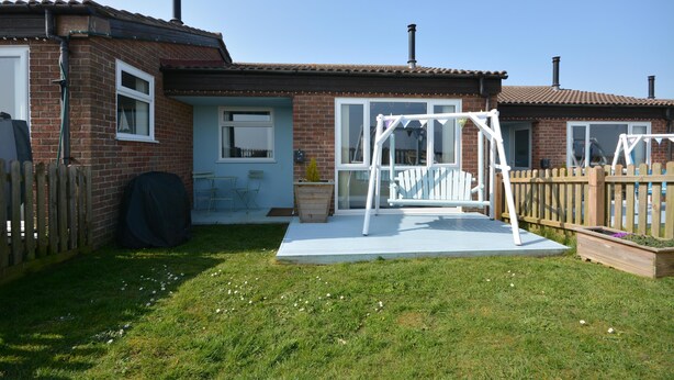 Ein Haus mit Backsteinfassade, einer überdachten Terrasse, einer Schaukel und einem eingezäunten Garten.