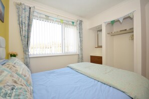 Un dormitorio con cama, cómoda, espejo y ventana con cortinas.