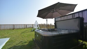 Ein Whirlpool mit einem großen Sonnenschirm, einem weißen Stuhl und einem Holzzaun im Hintergrund.