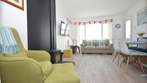 Ein Wohnzimmer mit Sofa, Sesseln, Tisch, Kamin und einem Fenster mit Vorhängen.