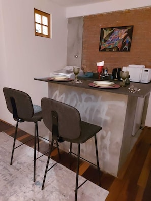 A small kitchen with a dining area, featuring a microwave, a sink, and a painting on the wall.