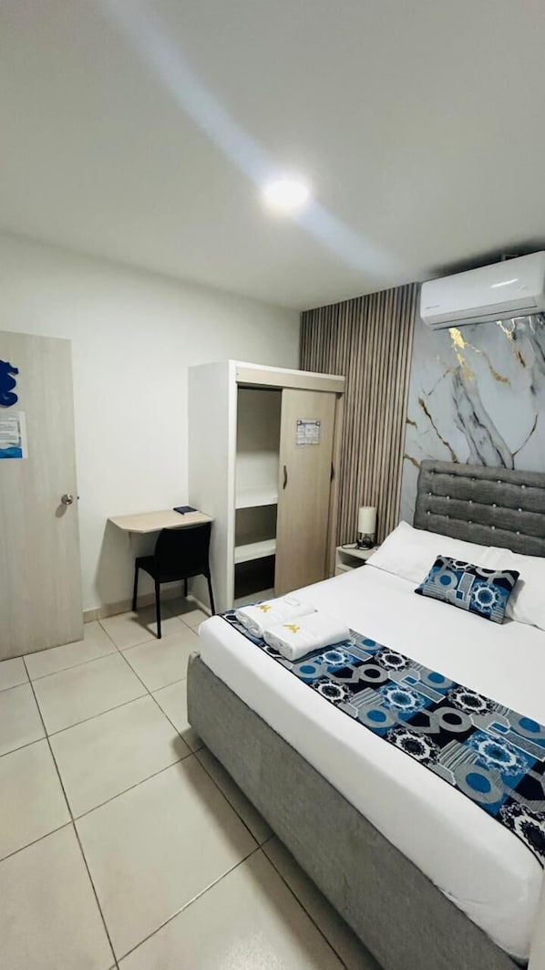 A hotel room with a bed, a desk, a wardrobe, and a wall-mounted air conditioner.