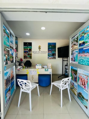 A reception desk with a logo, a TV, and two white chairs.