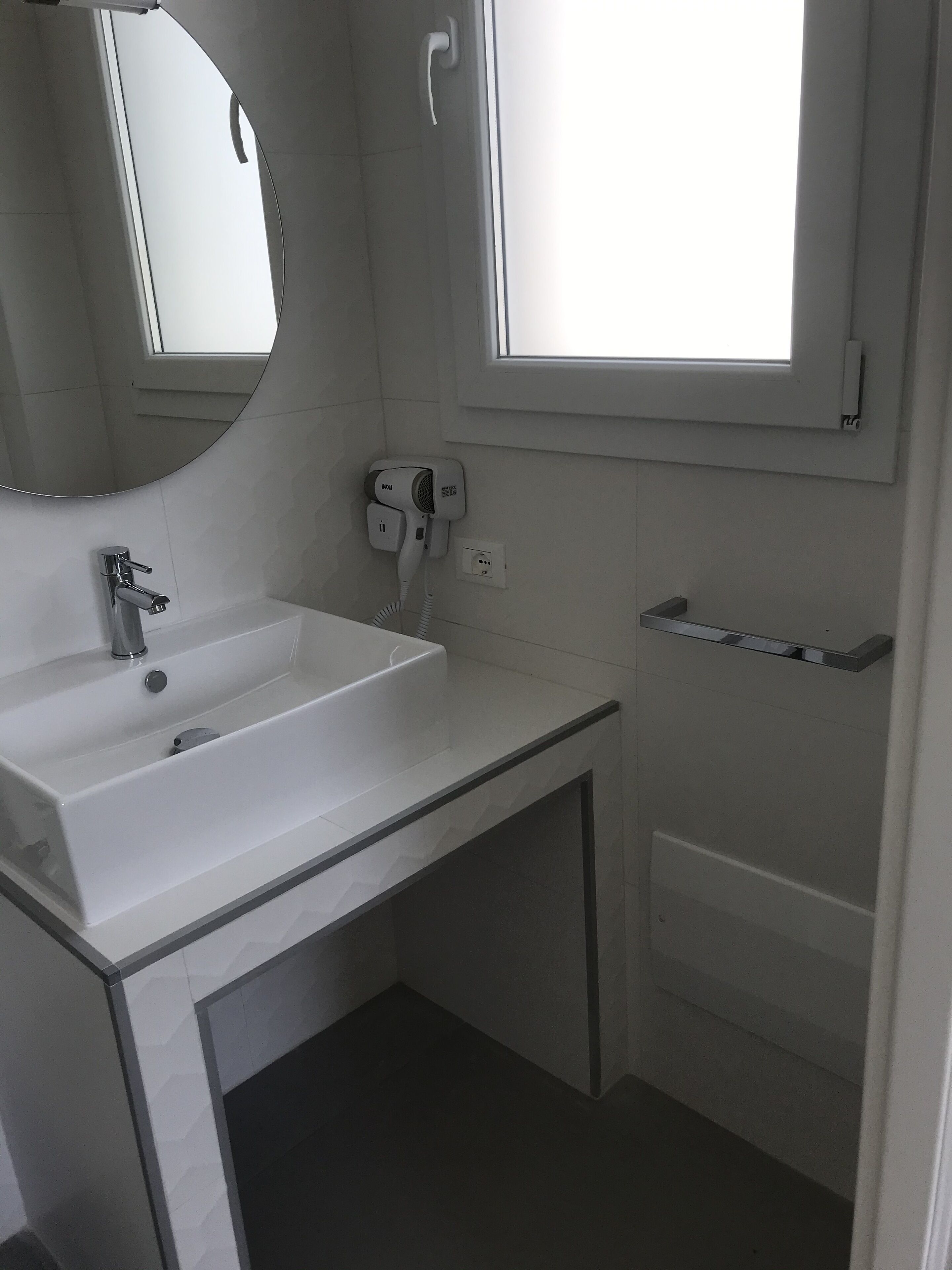 A modern bathroom with a white sink, mirror, and a window providing natural light.