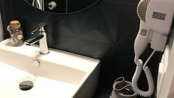 Une salle de bain avec un lavabo blanc, un sèche-cheveux et un petit plateau en bois contenant des articles de toilette.