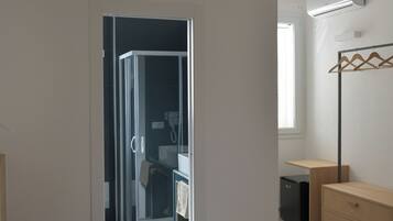 A bedroom with a bed, a wooden dresser, a walk-in closet, and a bathroom with a shower and toilet.