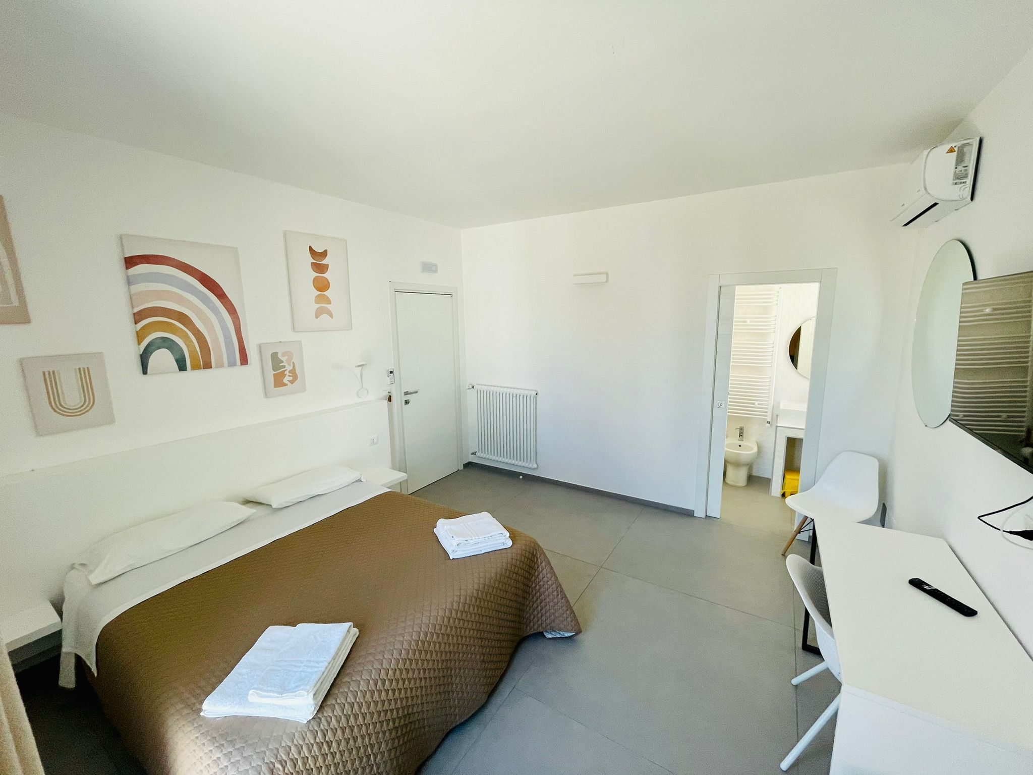 A hotel room with a bed, a desk, and a chair. There is a door leading to a bathroom.