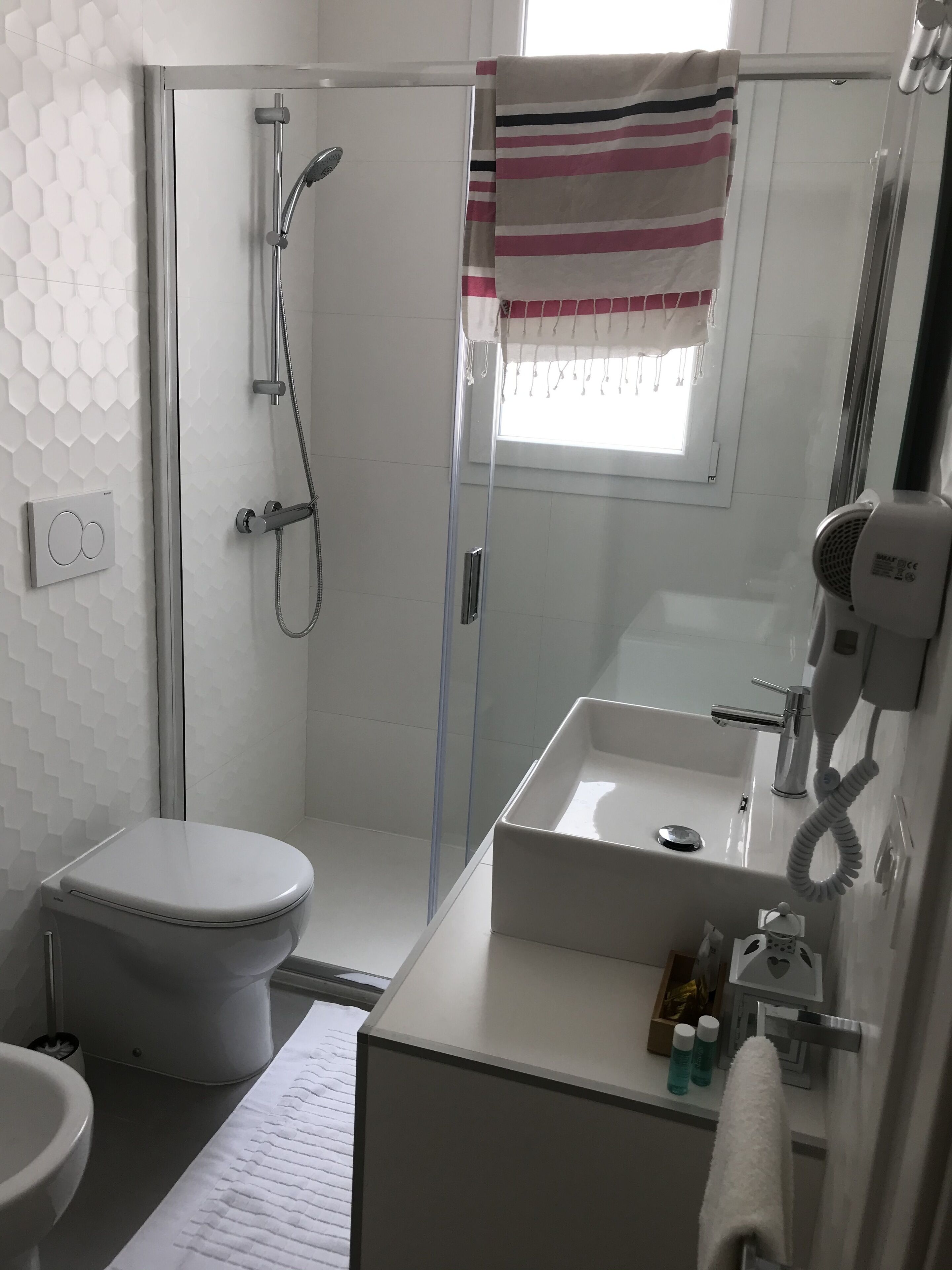 Ein modernes Badezimmer mit einer begehbaren Glasdusche, Toilette, Waschbecken mit Spiegel und Handtuchhalter.