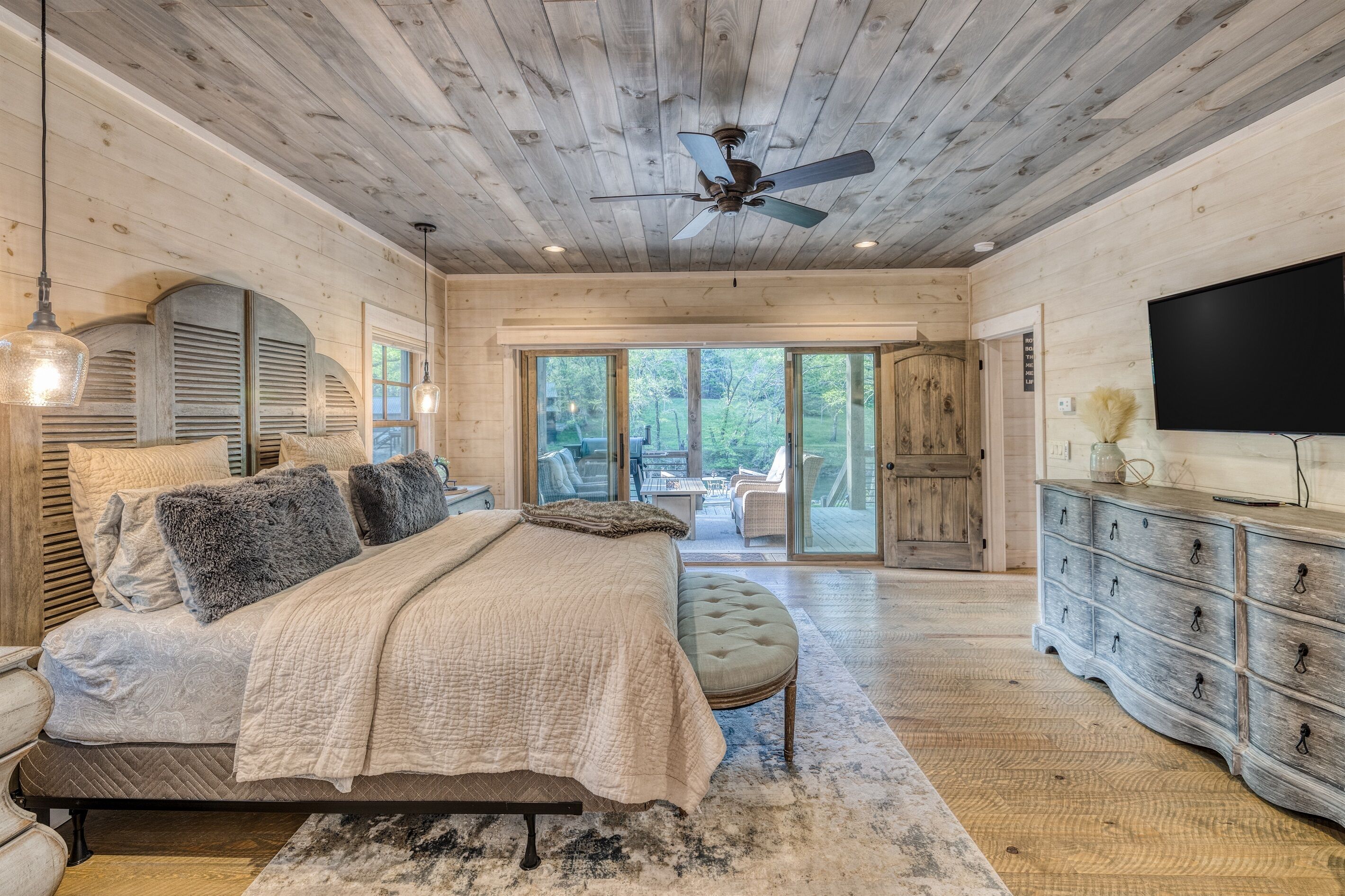 A spacious bedroom with a large bed, a dresser, and a TV.
