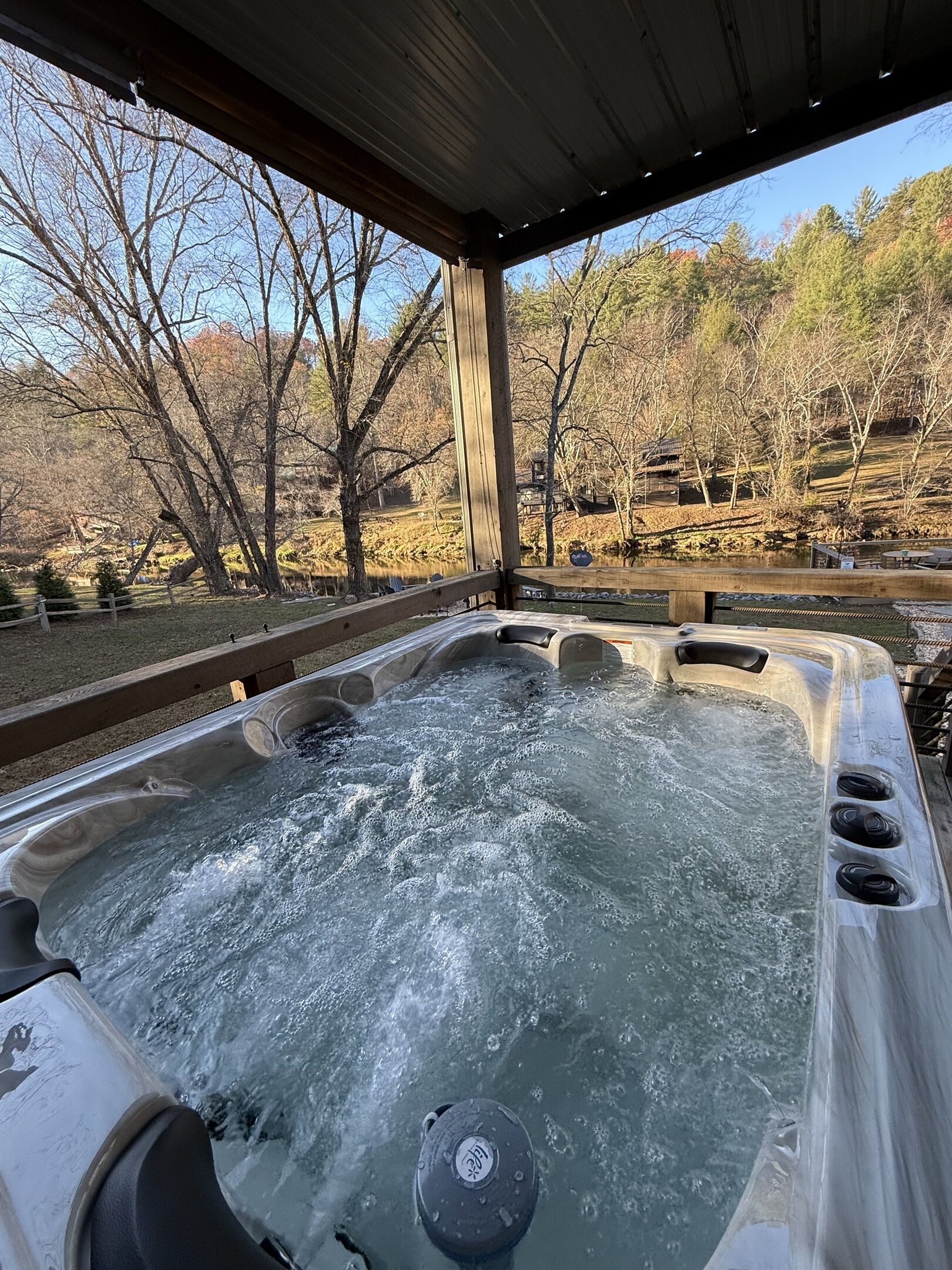 A hot tub with a wooden deck and a view of trees and a lake.