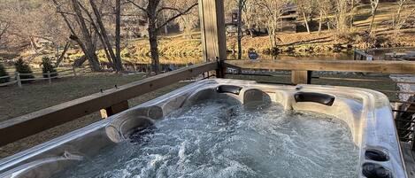 A hot tub with a wooden deck and a view of trees and a lake.