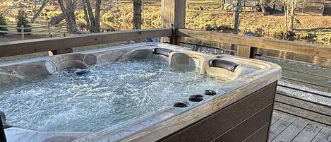 Ein Whirlpool mit einer Holzterrasse und Stufen, umgeben von Bäumen und einem Holzzaun.