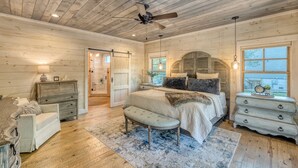 A bedroom with a wooden ceiling, a bed with a bench, a dresser, and a nightstand.