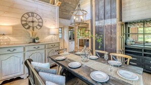 A rustic dining area with a wooden table set for four, a large wall clock, and a hanging light fixture.