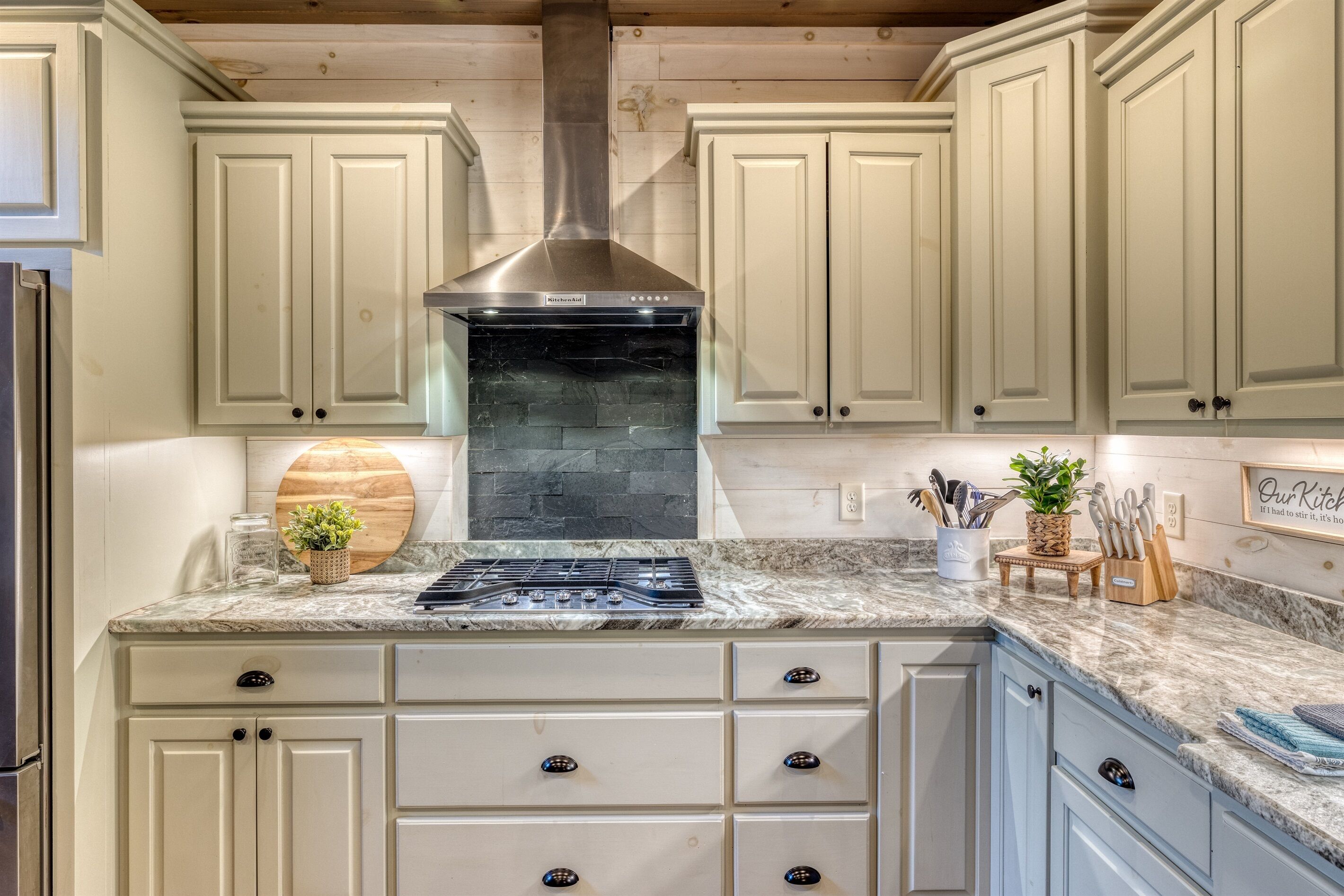 A kitchen with white cabinets, a stainless steel range hood, a granite countertop, and a built-in stove.