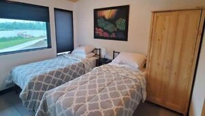 A room with two beds, a ceiling fan, a window with a view, and a wooden door. - Move-in ready lakeside retreat (Minerva)