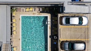 Ein Blick von oben auf einen Poolbereich auf einem Dach, mit zwei geparkten Autos rechts, umgeben von Liegestühlen und einem Pool.
