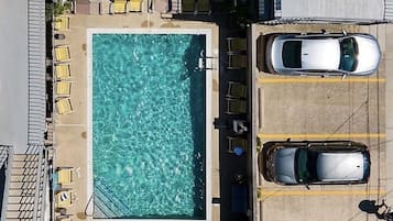 An aerial view of a rooftop pool area with two cars parked on the right, surrounded by lounge chairs and a pool.