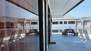 Ein überdachter Außenbereich mit weißen Plastikstühlen und -tischen, mit Blick auf eine Reihe weißer Gebäude.