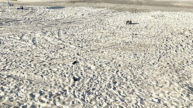 Ein weiter Sandstrand mit Fußspuren und einem bunten Sonnenschirm.