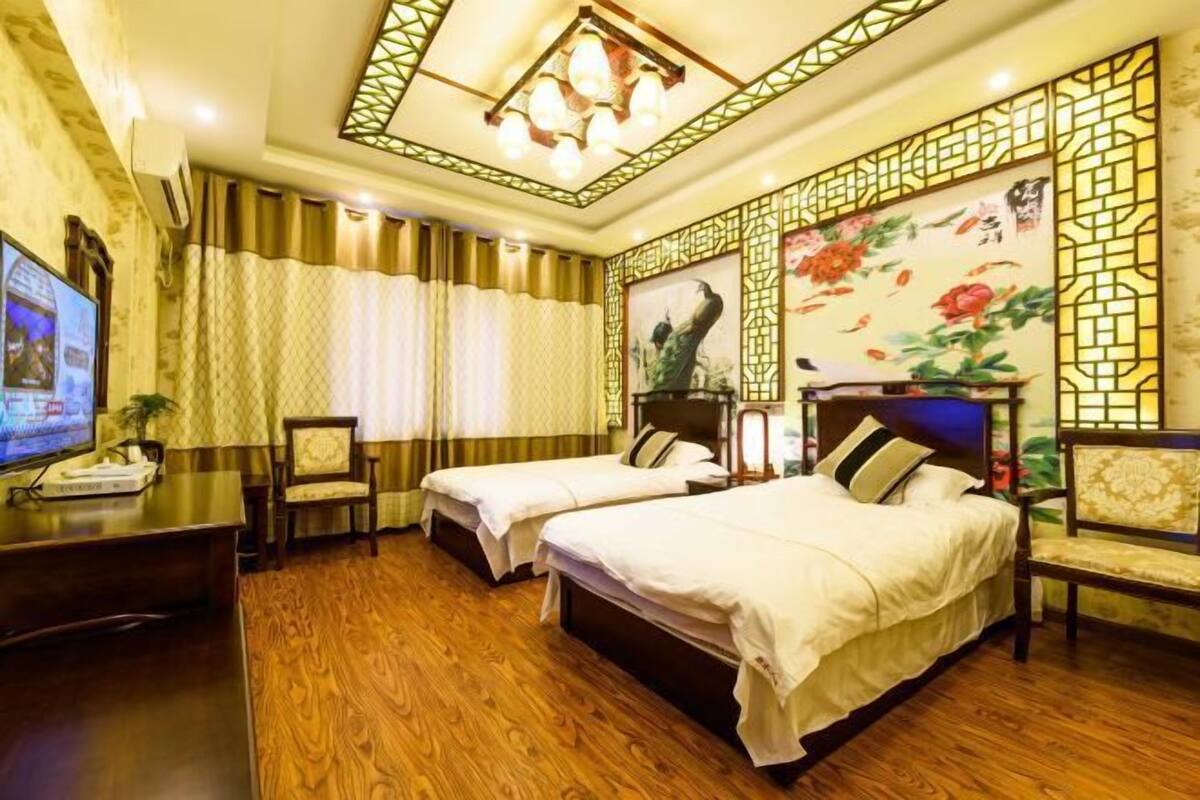 A hotel room with two beds, a desk with a television, and a decorative wall with a floral painting.