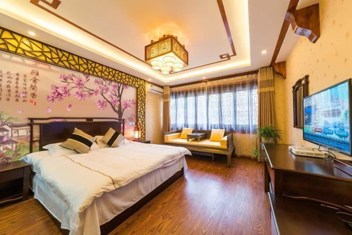 A modern hotel room with a large bed, a sofa, a TV, and a decorative wall with traditional artwork.