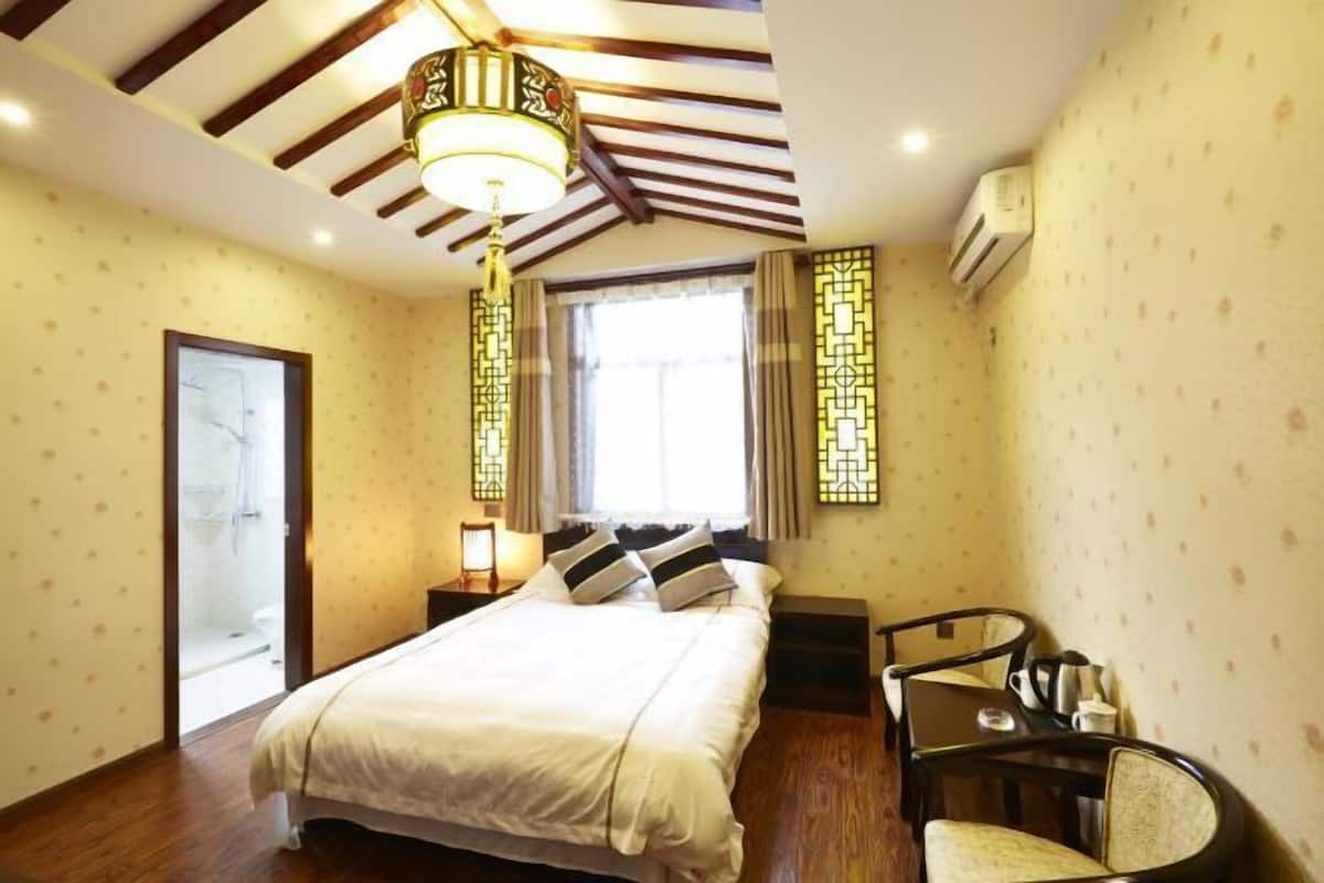 A hotel room with a bed, a desk, and a chair. There is a window with curtains and a ceiling fan.