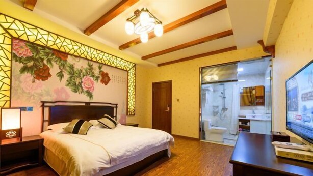 A bedroom with a bed, wooden floor, a TV, and a bathroom visible through a glass door.