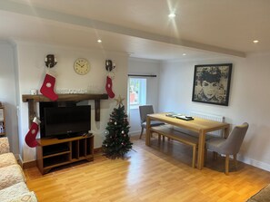 A living room with a TV, wooden entertainment unit, Christmas decorations, a dining table with chairs, and a radiator.